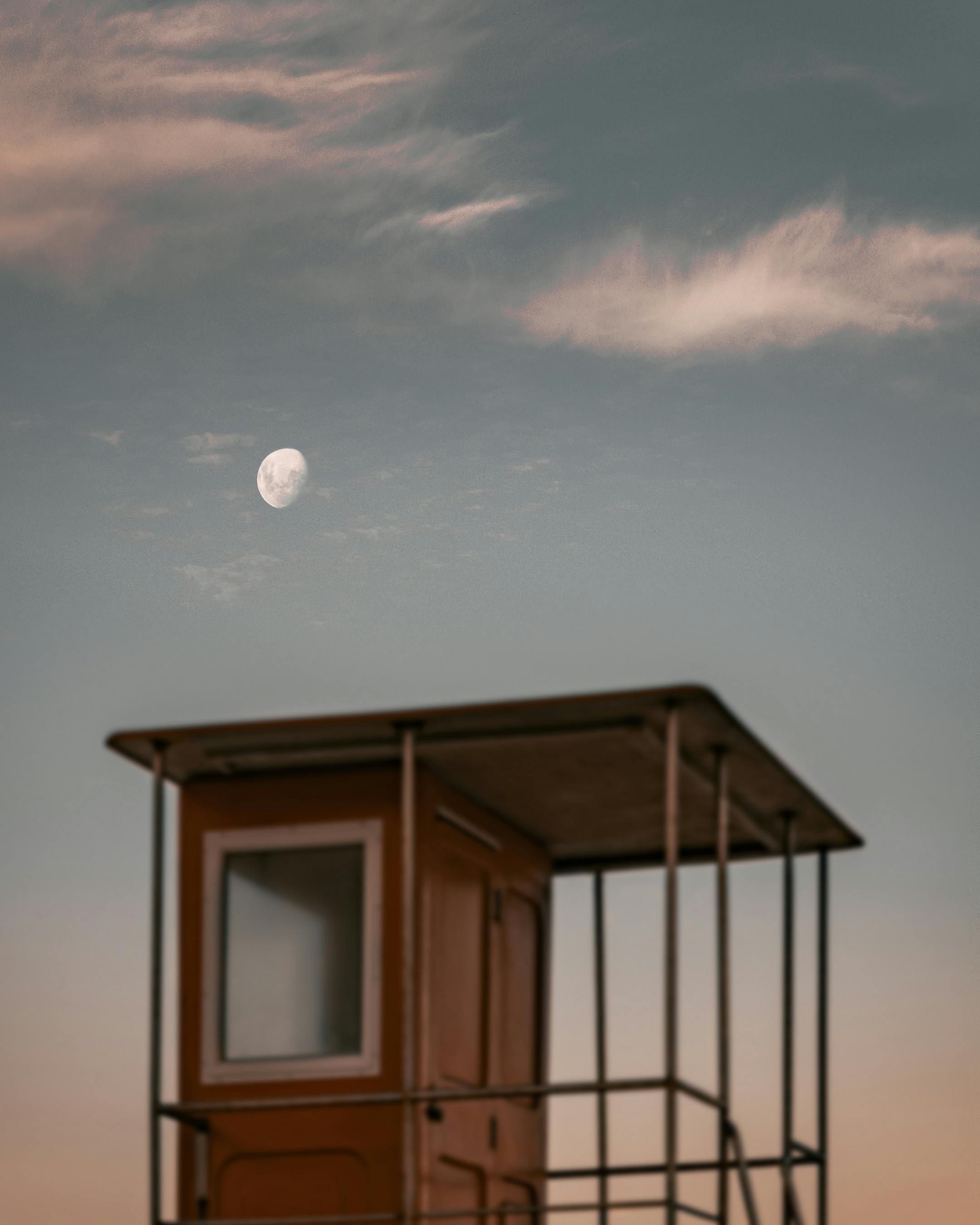 Gibbous moon and cirrus clouds over a lifeguard tower in Cape Town at twilight.