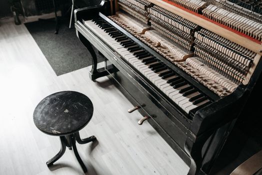 A detailed view of an open piano's inner mechanics with a wooden stool beside it.