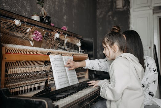 A young girl receiving piano lessons from a teacher. Indoor music education setting.