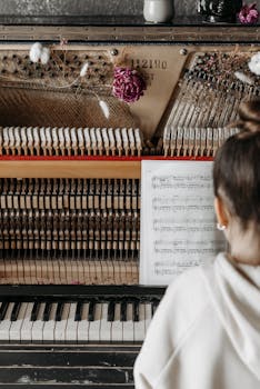 A detailed view of an upright piano with music sheet, adorned by flowers, and a female musician engaged in playing.