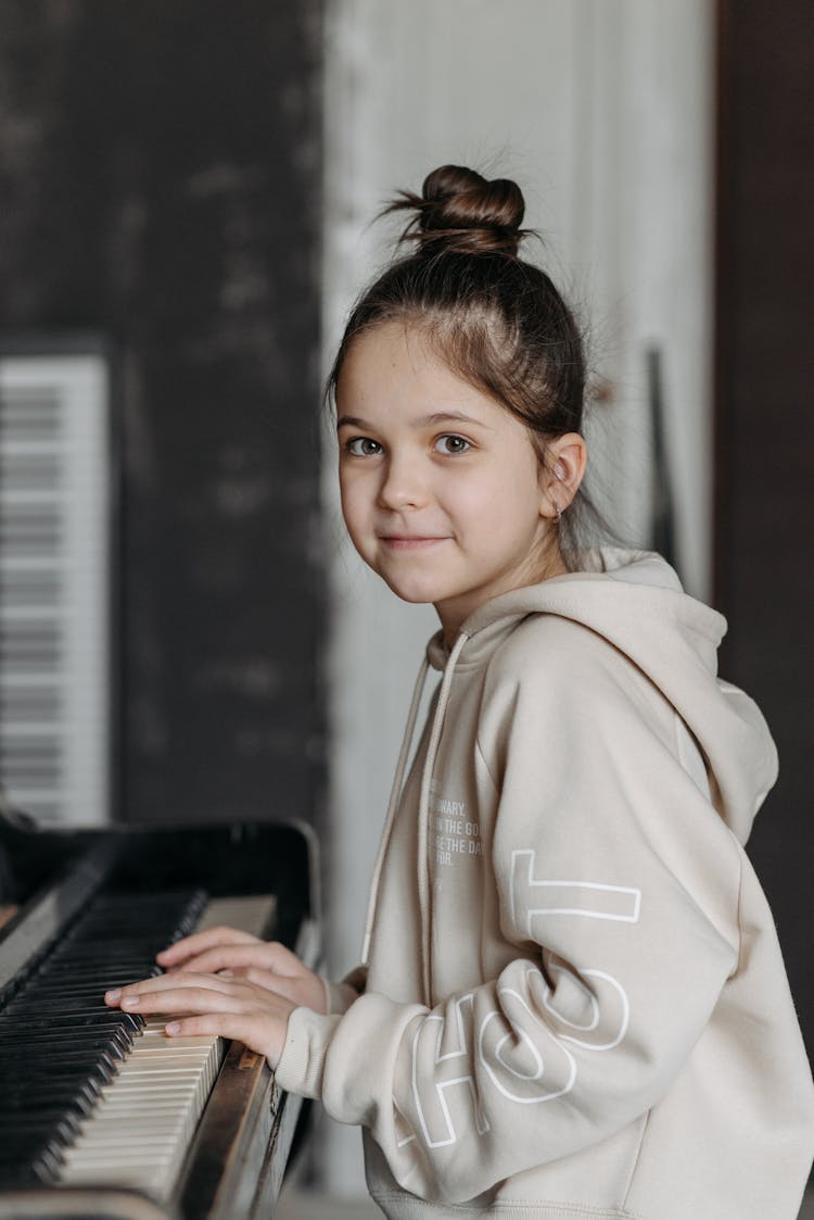 Girl In Beige Hoodie With Fingers On Piano Keys