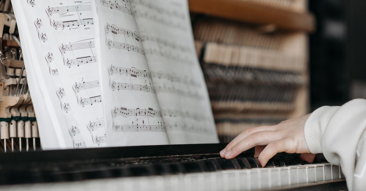close up of hands on piano keys, sheet music partially visible but out of focus