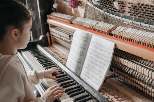 Free A young girl sits indoors playing piano while reading a music sheet, showcasing concentration and musical training. Stock Photo