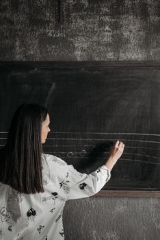 A music teacher writing musical notation on a blackboard indoors, focused on teaching.