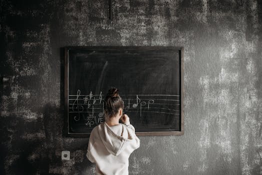 A student in a hoodie learns music notation on a chalkboard in class.