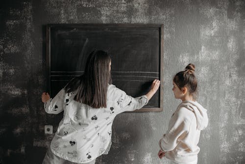 Teacher Writing on a Blackboard Beside a Student