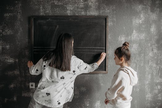 A teacher writing on a chalkboard during a private lesson with a child student indoors.