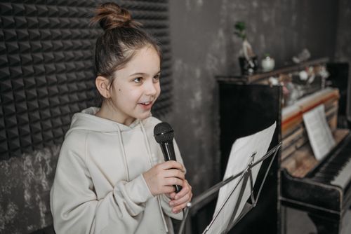 Free Caucasian girl singing into a microphone in a soundproof studio with sheet music and piano. Stock Photo