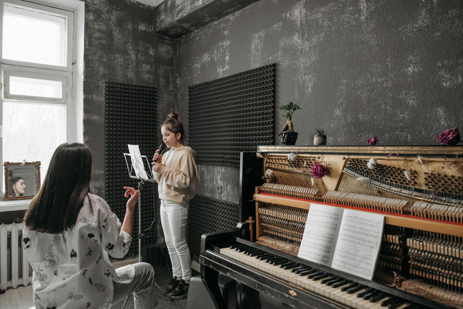 A young girl takes a vocal lesson in a soundproof music studio with her teacher.