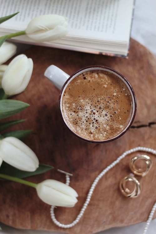 Mug of cacao with classy accessories and tulips bouquet placed on tray near book