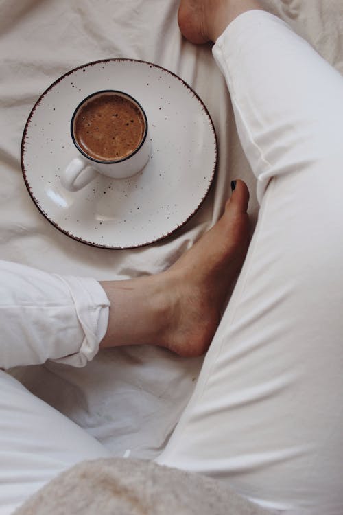 Free From above of crop anonymous barefooted female relaxing on comfortable bed near cup of freshly prepared aromatic cacao Stock Photo
