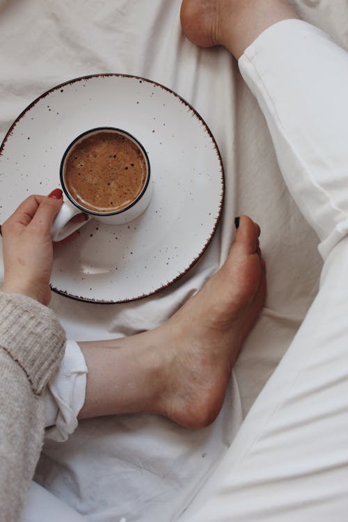 Free Crop unrecognizable woman relaxing on bed and drinking hot cacao Stock Photo