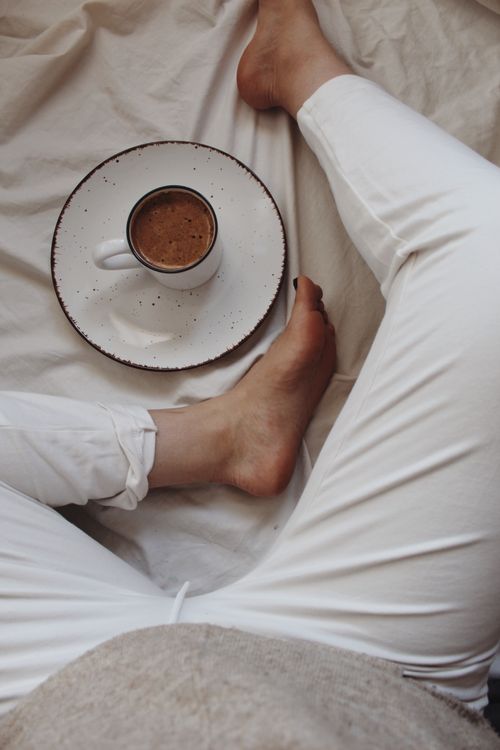 Free High angle of cup of hot aromatic cacao placed on soft bed near crop anonymous barefooted woman relaxing during weekend at home Stock Photo
