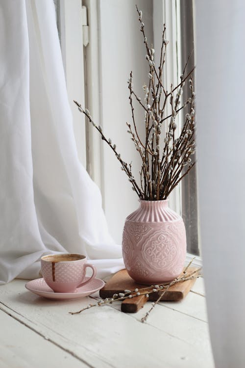 Cup of aromatic chocolate with vase of pussy willow placed on windowsill