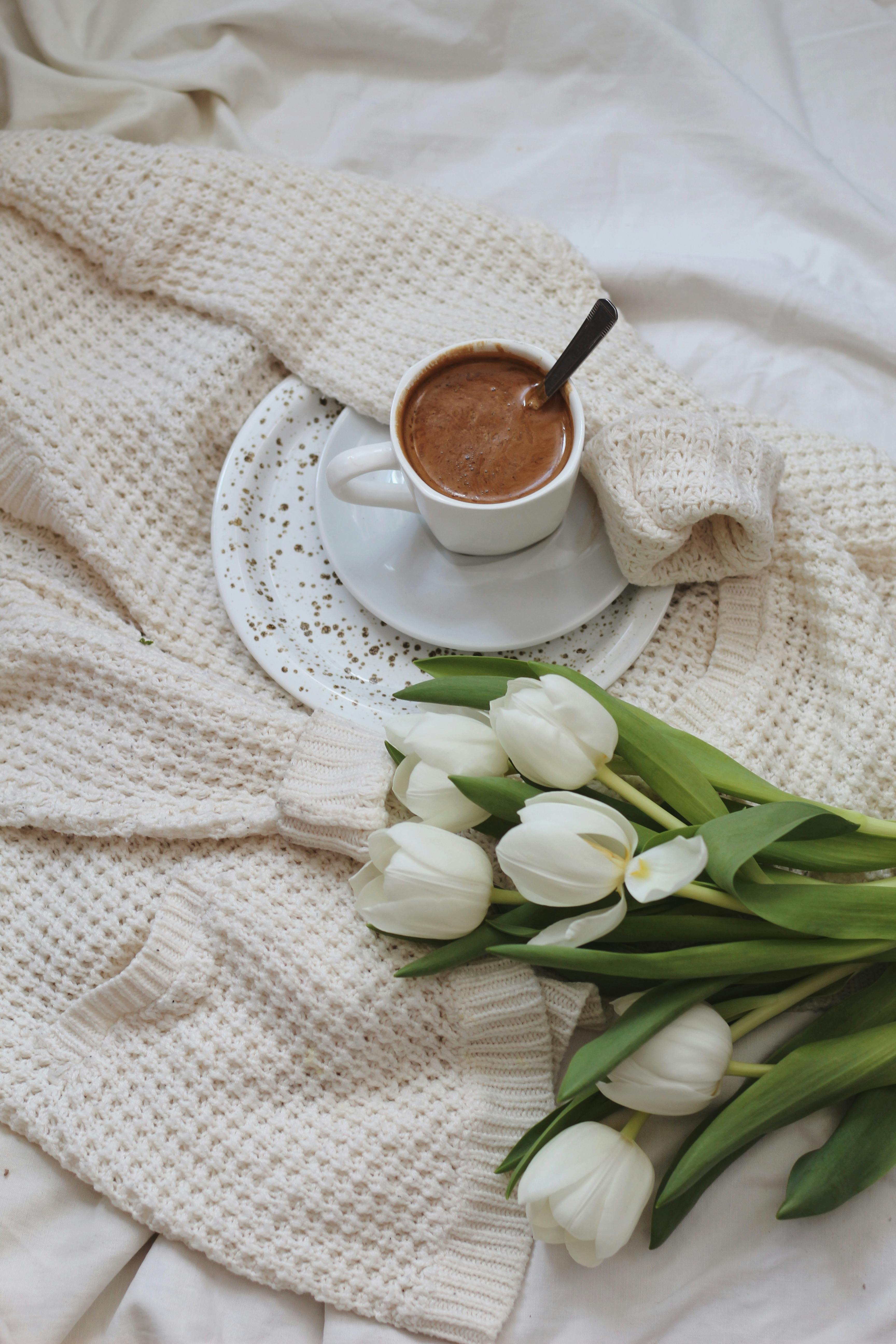 Flowers and cup of cacao placed on knitted cardigan on bed · Free Stock ...