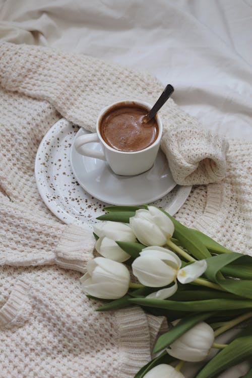 Free Cup of coffee with bunch of tulips and sweater on bed Stock Photo