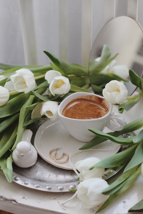 Free From above of elegant necklace and golden earrings placed on saucer near cup of foamy cacao served on silver tray with bunch of white tulips on table Stock Photo