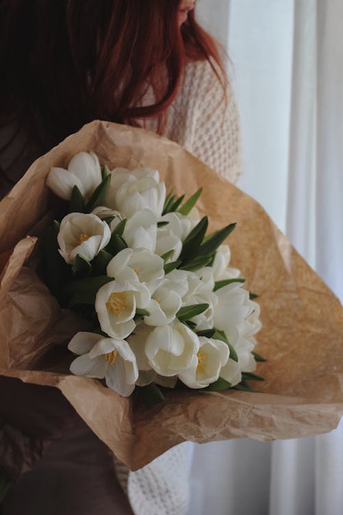 Unrecognizable woman standing near window with bunch of tulips