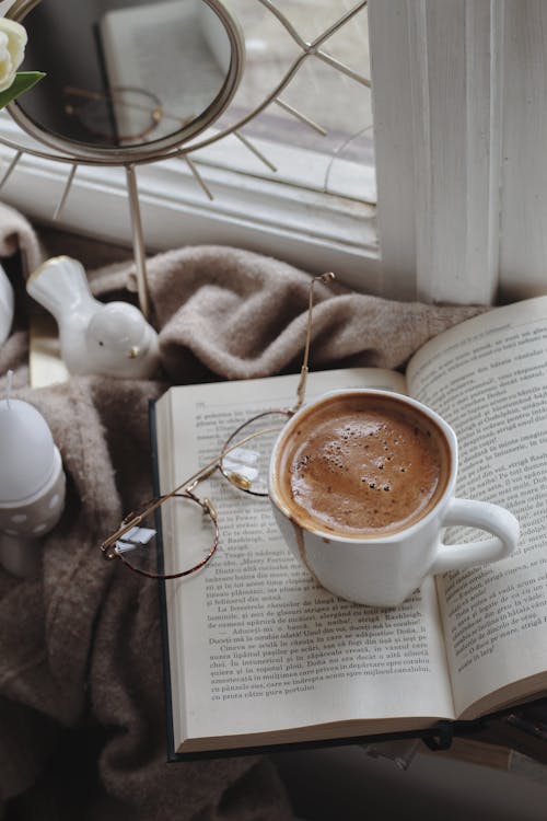 Free Coffee cup with book and eyeglasses arranged on warm plaid on windowsill Stock Photo