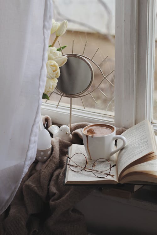 Free Cup of coffee with book and flowers placed on plaid on windowsill Stock Photo