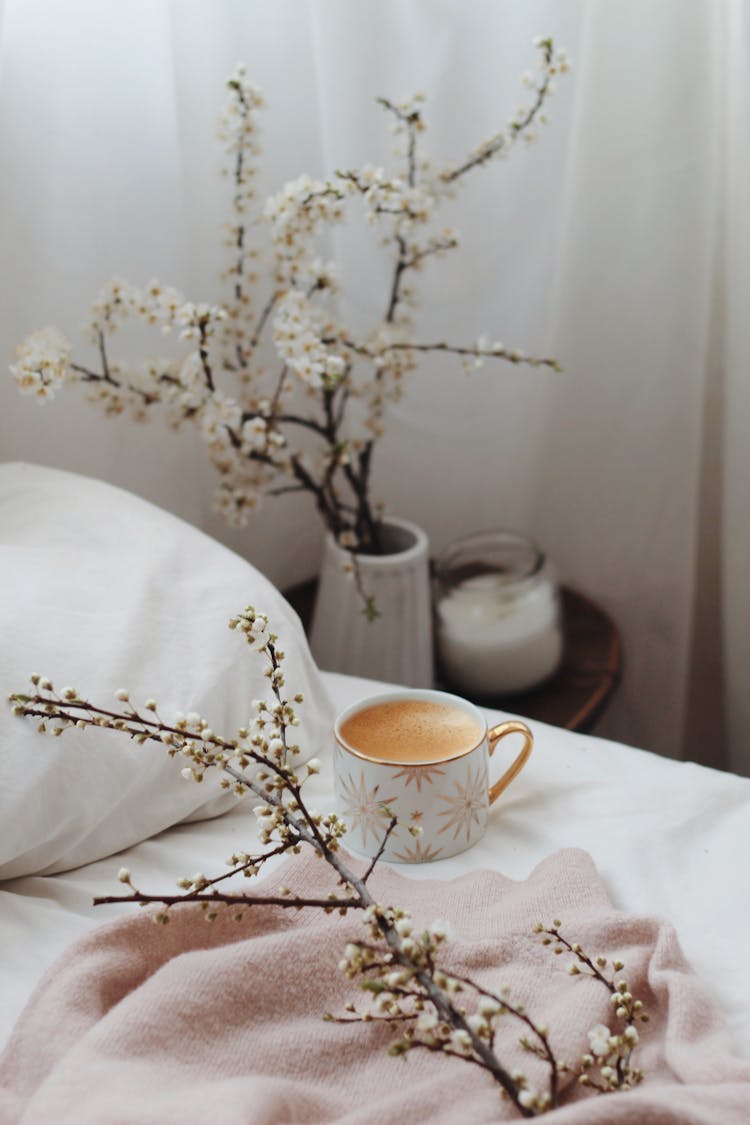 Cup Of Cappuccino Placed On Cozy Bed Near Nightstand With Flowers Vase