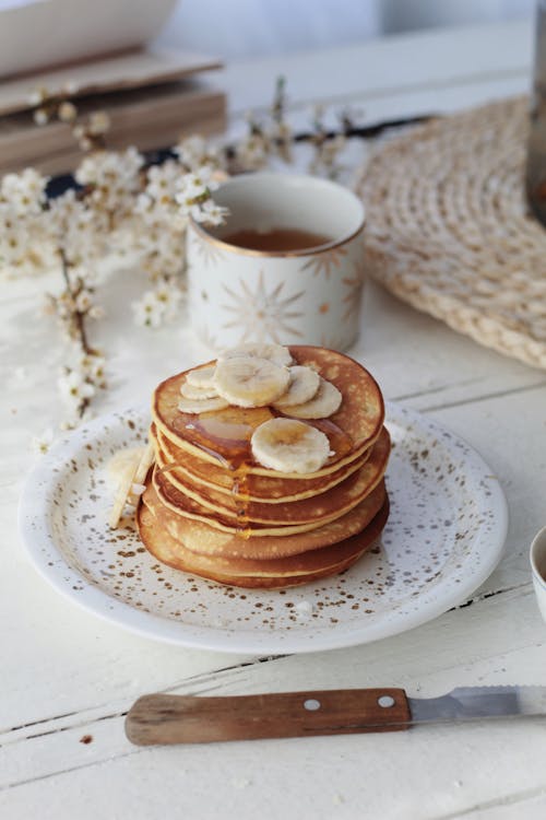 Free From above stack of yummy sweet pancakes topped with bananas and syrup served on plate on table with cup of tea in morning Stock Photo