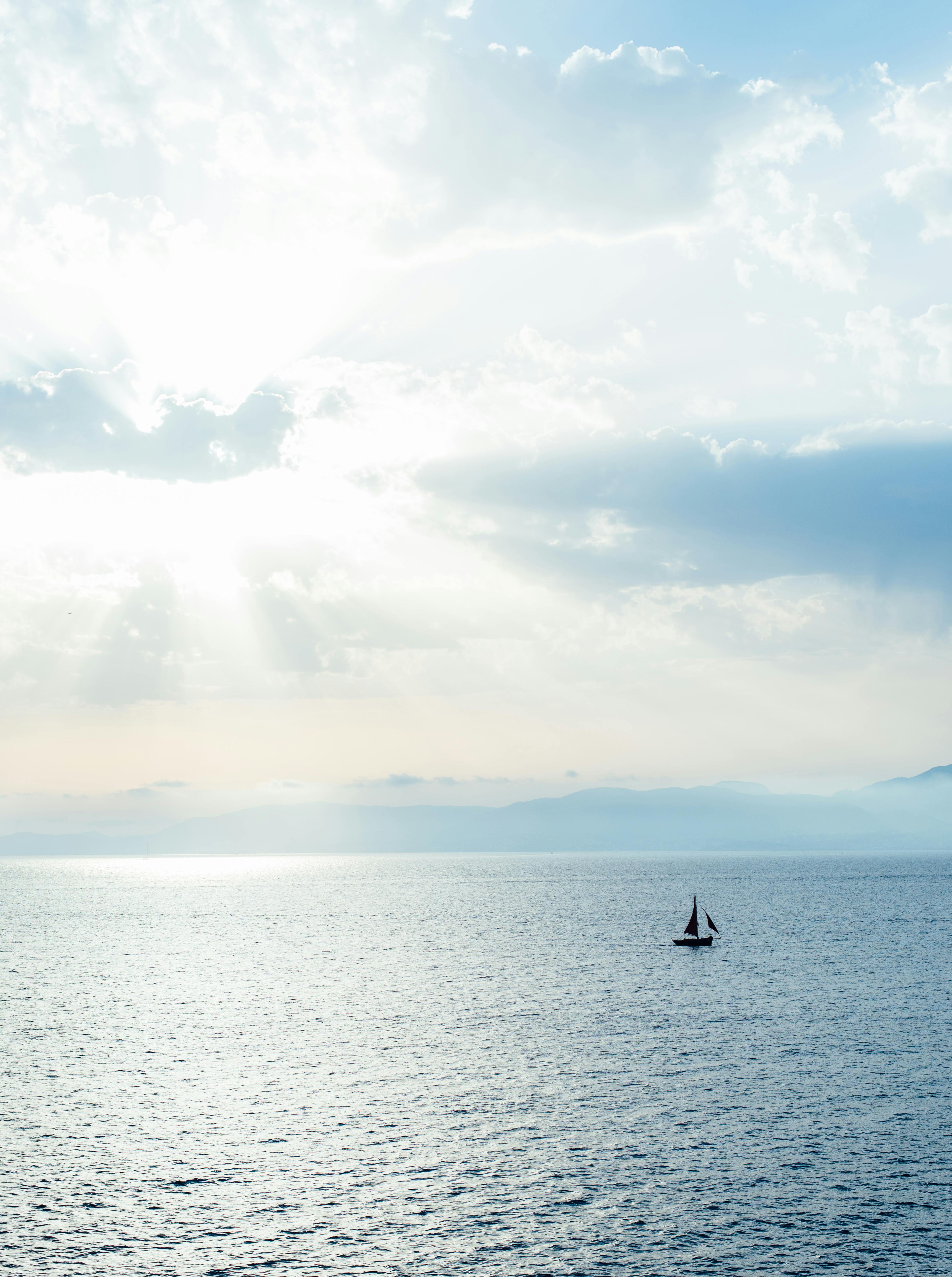 A serene seascape with a solitary sailboat under a bright sky in Spain.