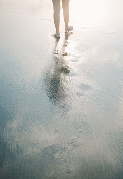 Free A person walks along the beach, leaving footprints in the wet sand under the morning sun. Stock Photo