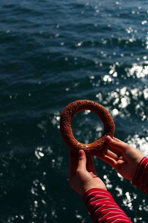 Free From above of crop anonymous person holding sweet bagel in hands standing above sparkling seawater in sunlight Stock Photo