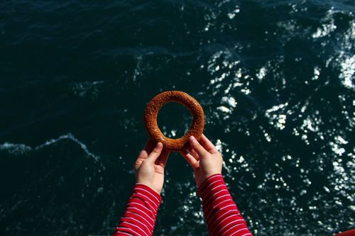 Free Top view of crop anonymous person reaching out hands with bagel above dark green sea in sunlight Stock Photo