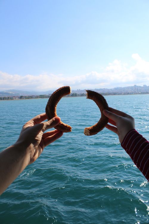 Free Crop person connecting halves of delicious bagel against calm sea and cloudy blue sky Stock Photo