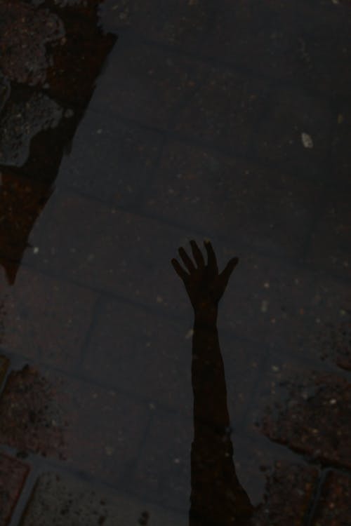 From above of shadow of anonymous crop person arm on shabby tile in dark