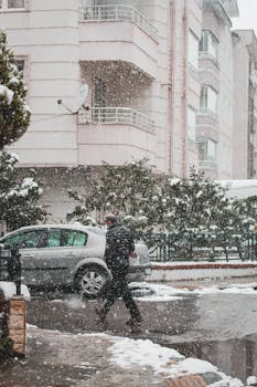 Unrecognizable man in warm clothes walking on roadside near residential buildings district in winter day