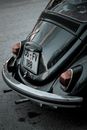 Back part of old fashioned black car with number plate on asphalt in daytime