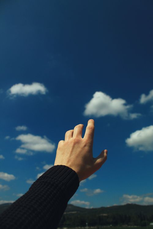 Free Crop unrecognizable male holding hand up stretching to bright blue sky with clouds in summer day Stock Photo