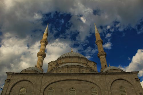 From below old stone mosque with dome and ornaments against cloudy blue sky on sunny day