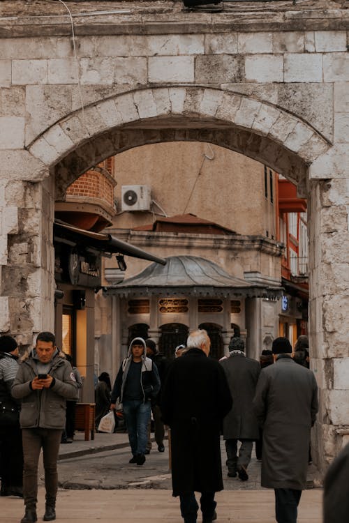 View of ancient street with stone archway and old buildings full of people in warm clothes in fall