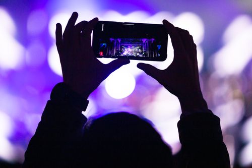 Free Silhouette of hands holding smartphone capturing a live concert with vivid purple lights. Stock Photo