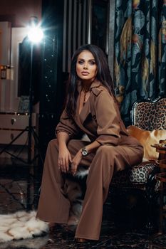 Fashionable woman in a modern studio, wearing a brown suit, sitting on a chair.