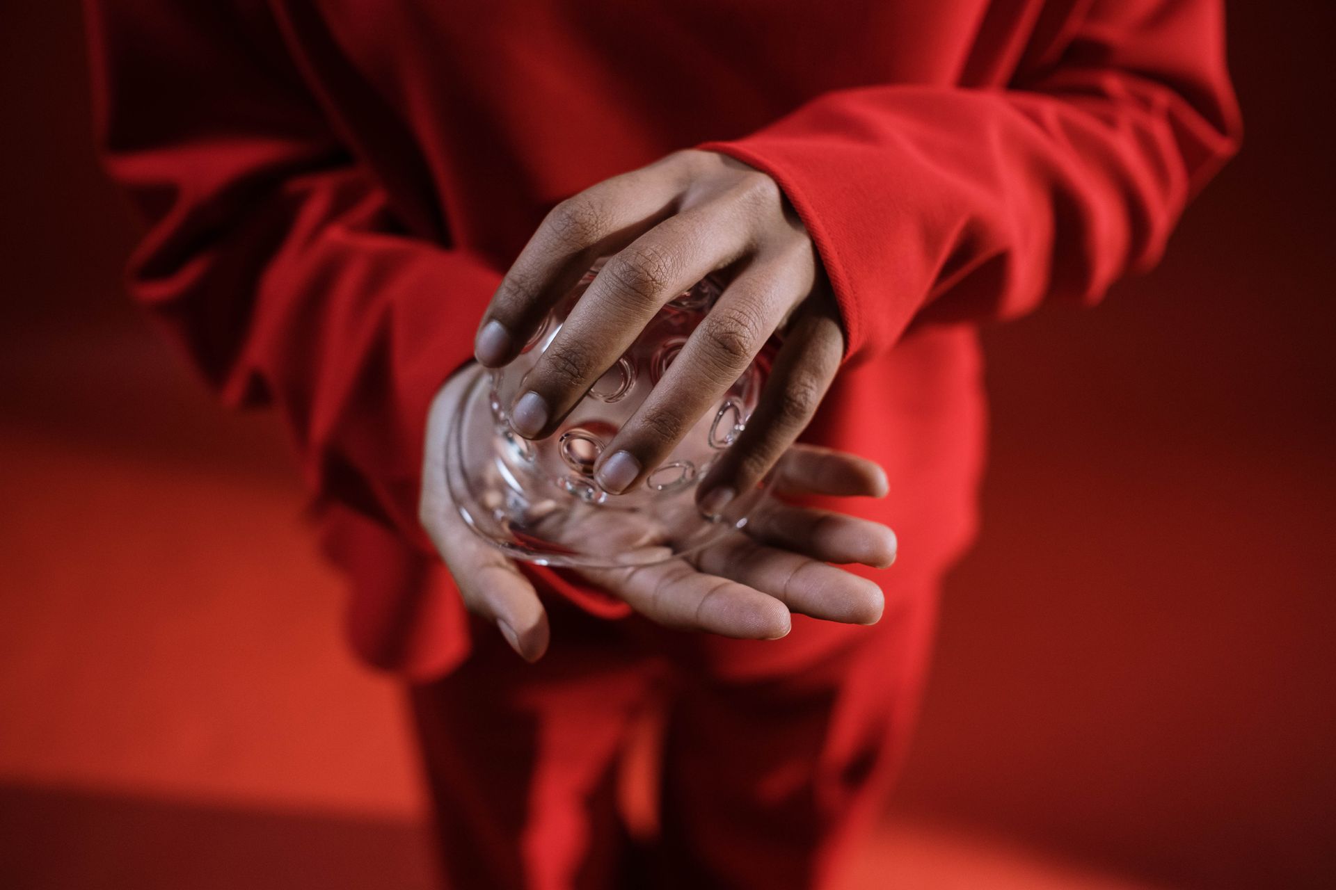 A person in red clothes holds a transparent glass object in their hands.