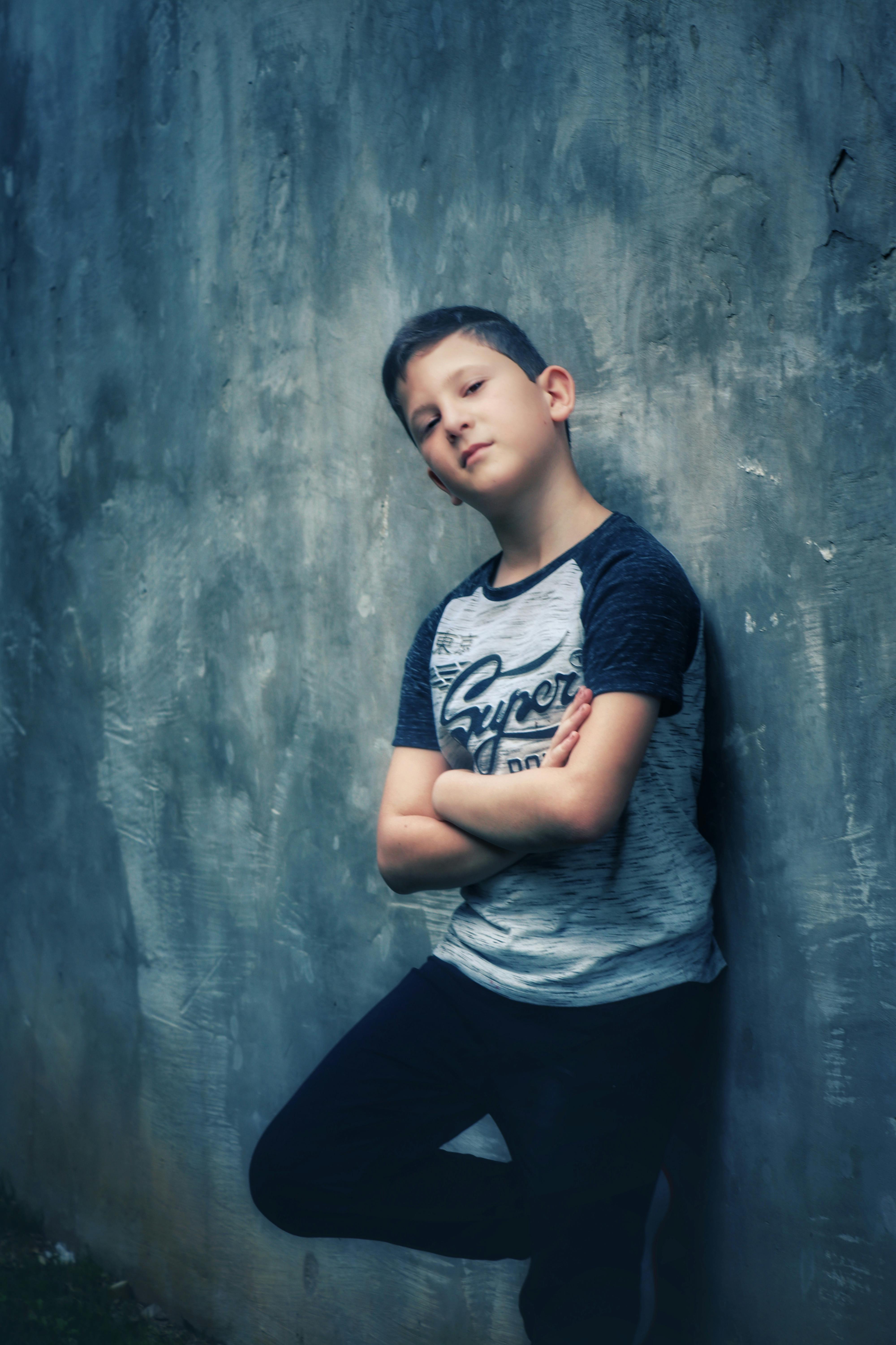 A young boy confidently poses with arms crossed against a textured concrete wall.