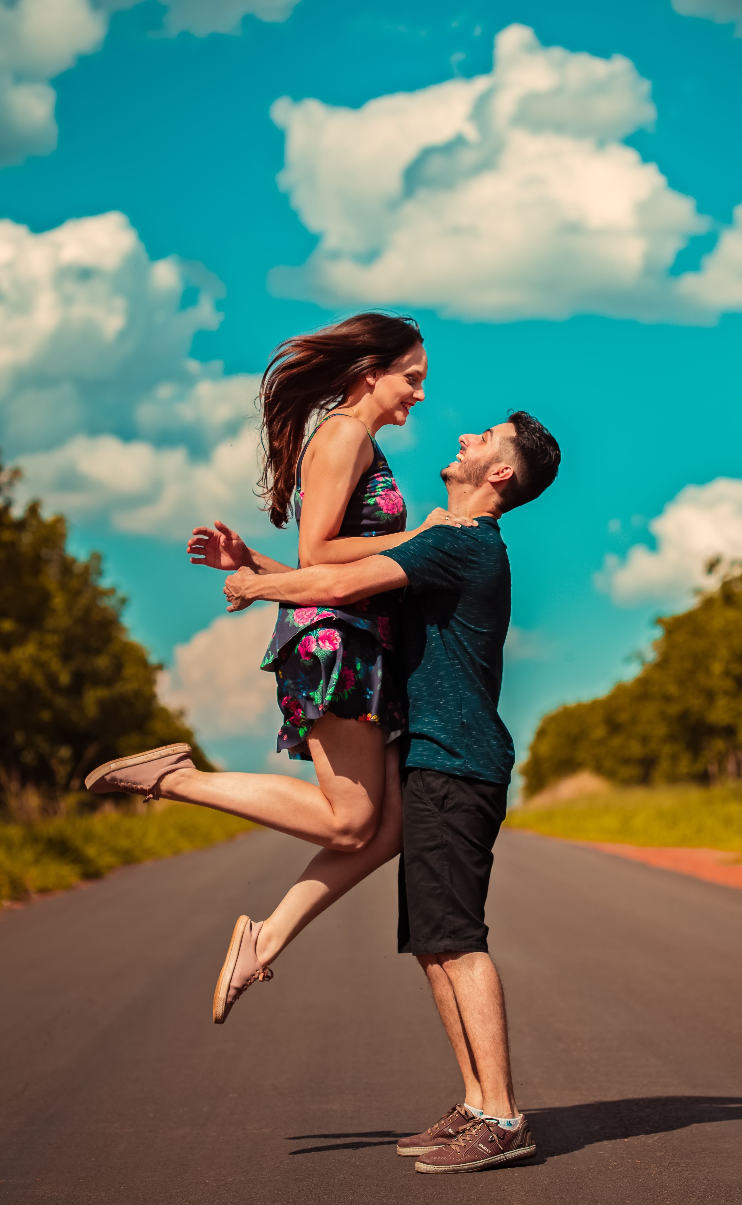 Happy couple embracing on a sunny road, capturing romance and joy against a bright blue sky.