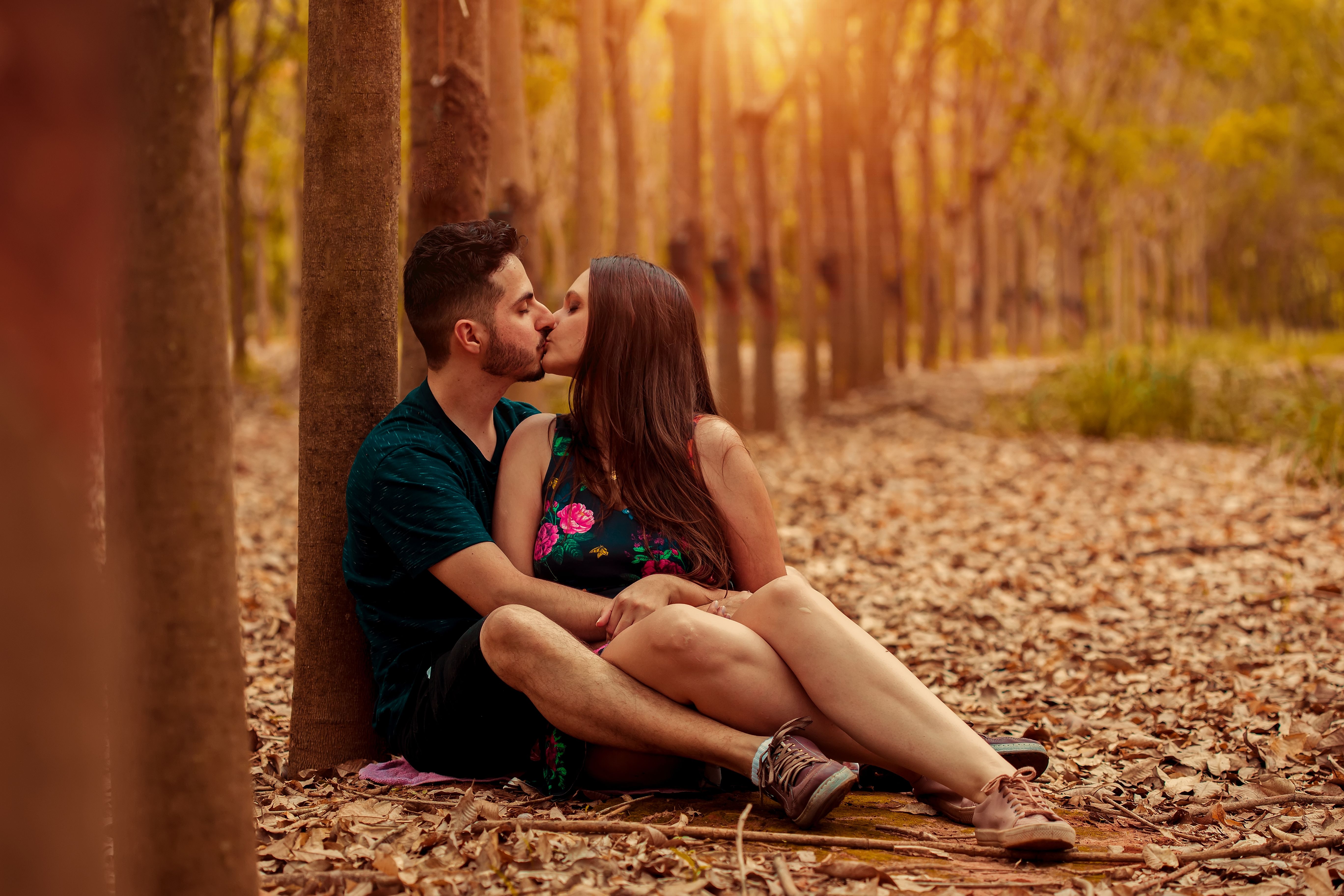 A loving couple sharing a kiss while seated among dried leaves in an autumn forest.
