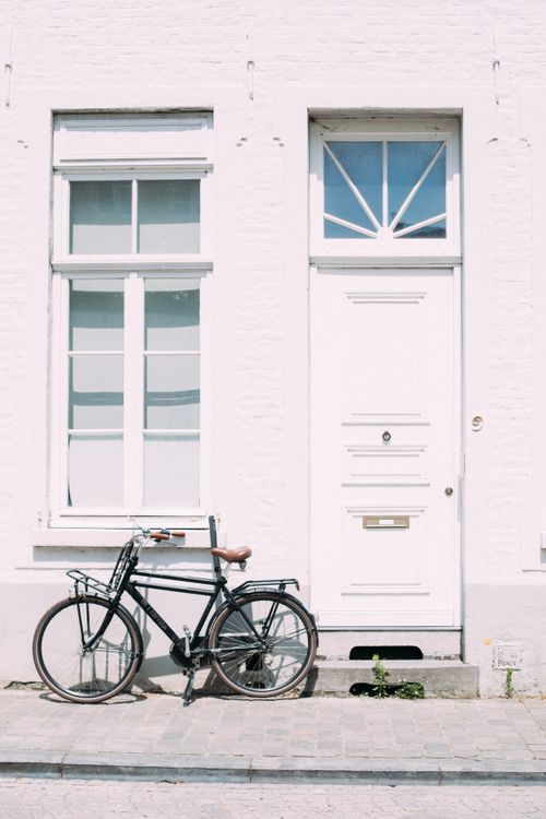 Free A vintage black bicycle parked by a classic white wall in sunny Bruges, Belgium. Stock Photo