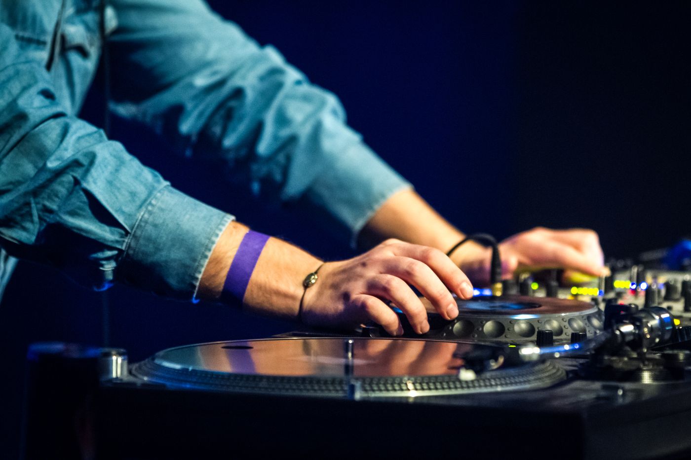 Hands on a turntable and mixer against a navy background