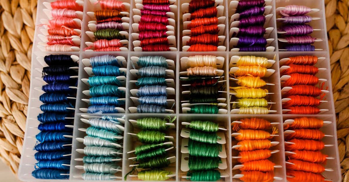 A well-organized box of vibrant embroidery threads arranged by color on a woven mat.