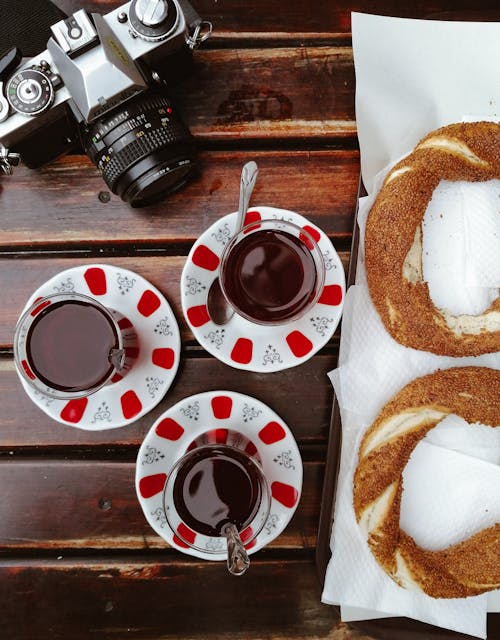 Black Dslr Camera on Brown Wooden Table Beside the Drinks and Breads