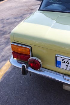 Rear bumper of vintage automobile with license plate and shadow on urban roadway in sunlight
