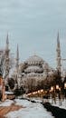 Sultan Ahmed Mosque exterior with towers against snowy walkway and lanterns under cloudy sky in Istanbul Turkey