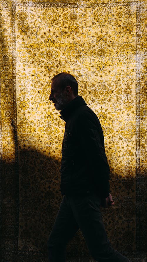 Side view of mature male with hand behind back strolling against rug with oriental pattern and shade on night street